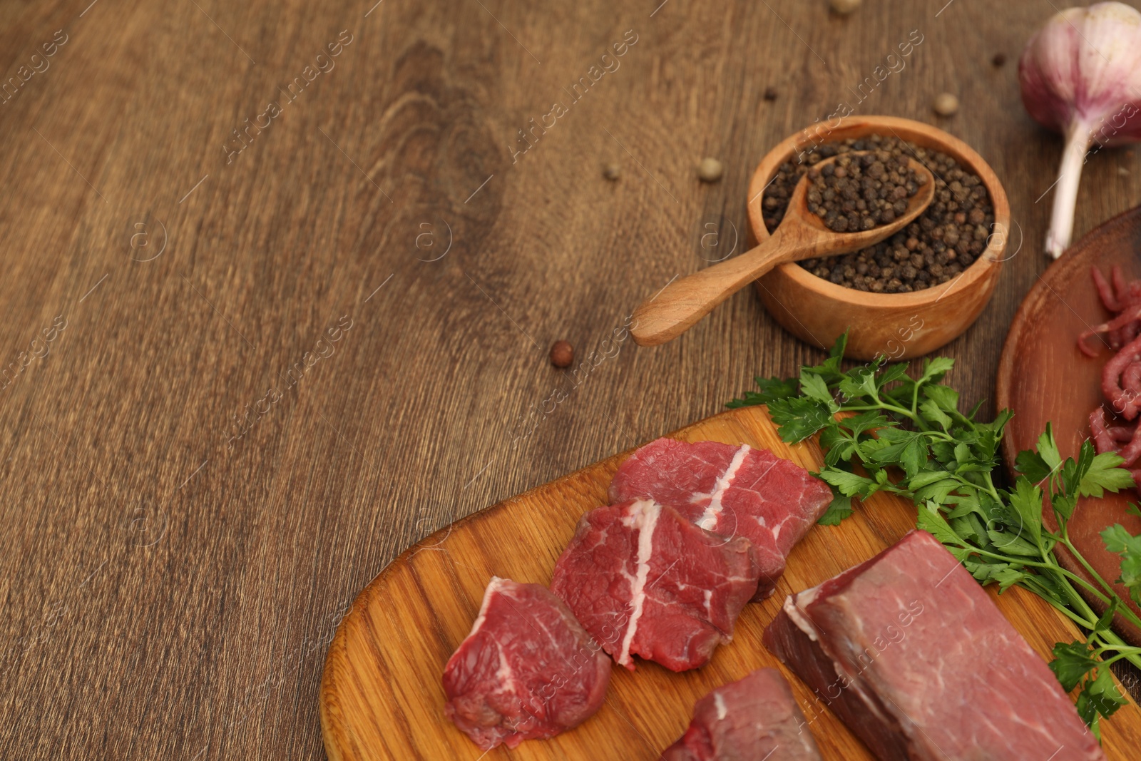 Photo of Beef, garlic, parsley and peppercorns on wooden table. Space for text