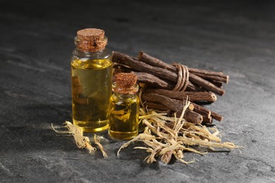 Dried sticks of licorice root and bottles with essential oil on black textured table