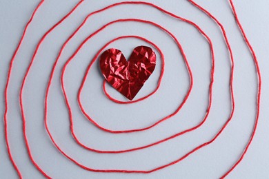 Red crumpled paper heart and thread on gray background, top view