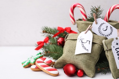 Photo of Bags with gifts, cookies and festive decor on white table, space for text. Christmas advent calendar