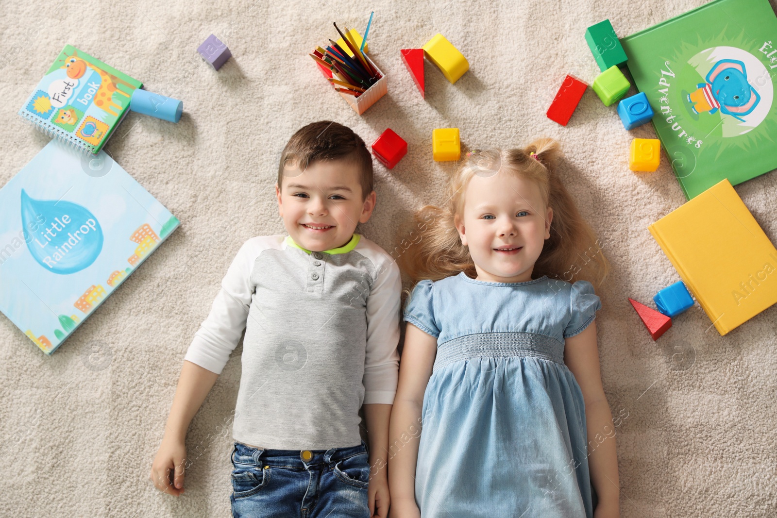 Photo of Little children with toys and books lying on carpet indoors, top view. Playtime