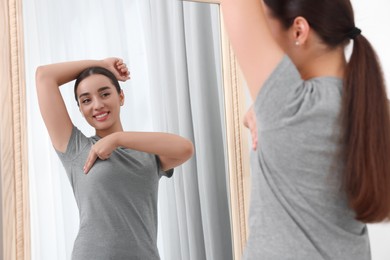 Beautiful happy woman doing breast self-examination near mirror indoors