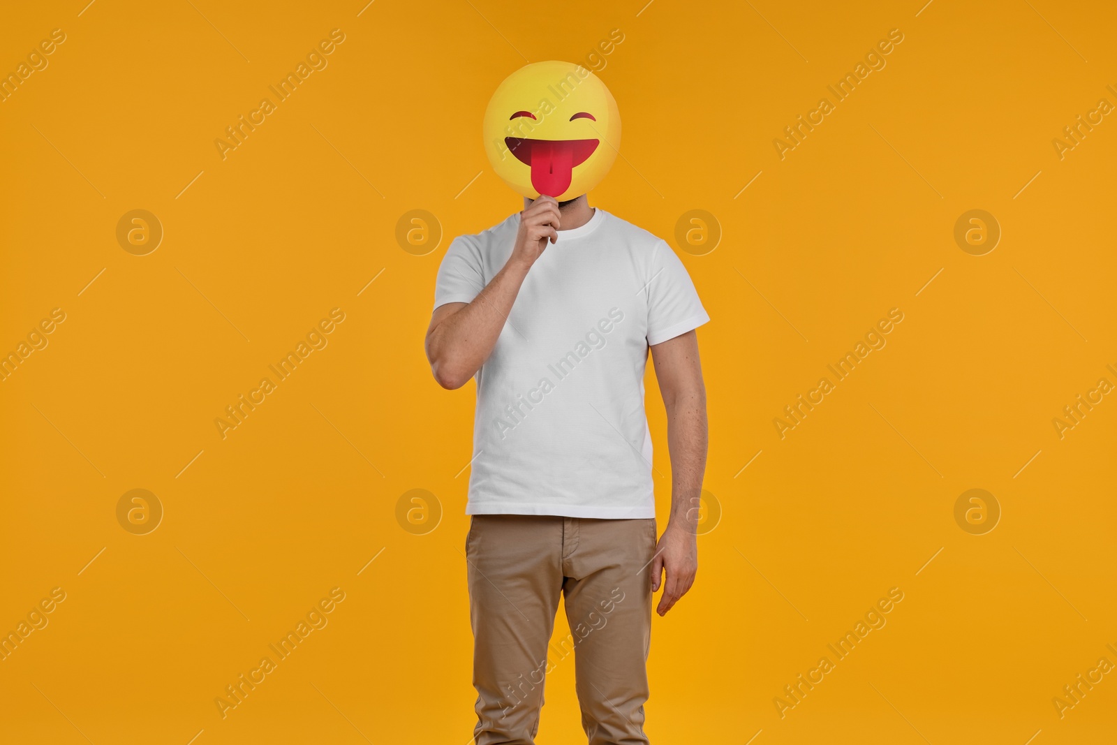 Photo of Man covering face with emoticon sticking out tongue on yellow background