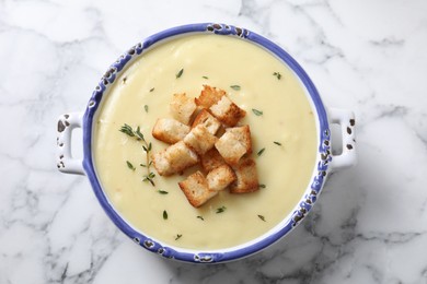 Tasty potato soup with croutons and rosemary in ceramic pot on white marble table, top view