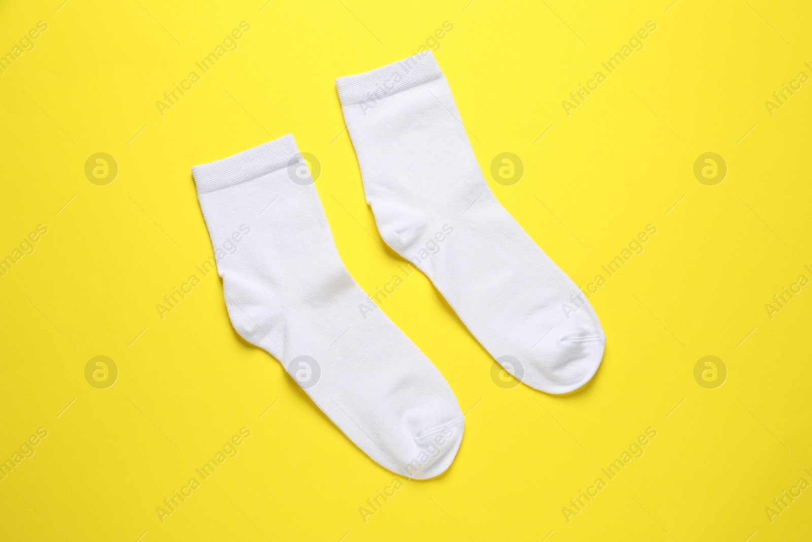 Photo of Pair of white socks on yellow background, flat lay
