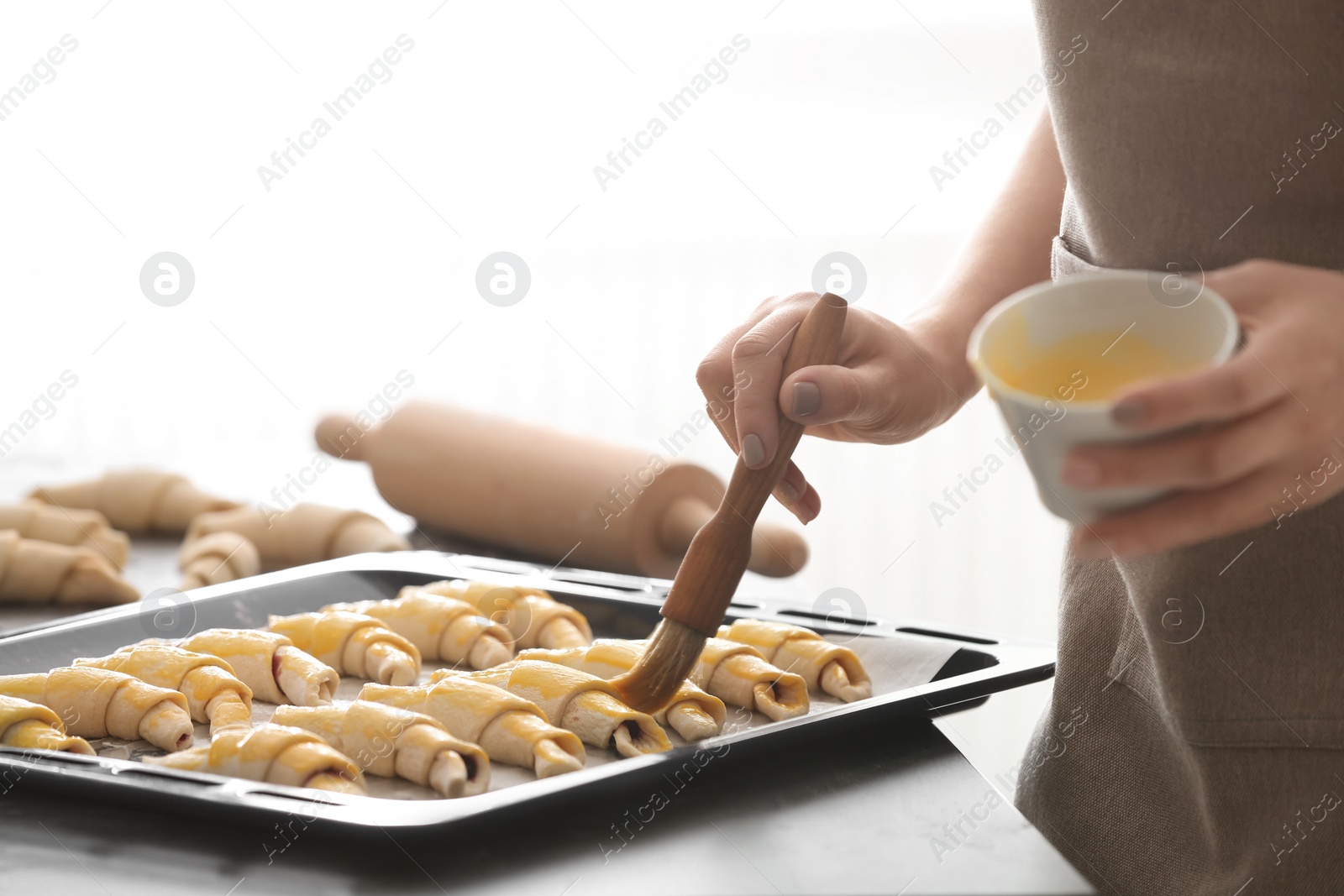 Photo of Woman spreading egg yolk on croissants, closeup