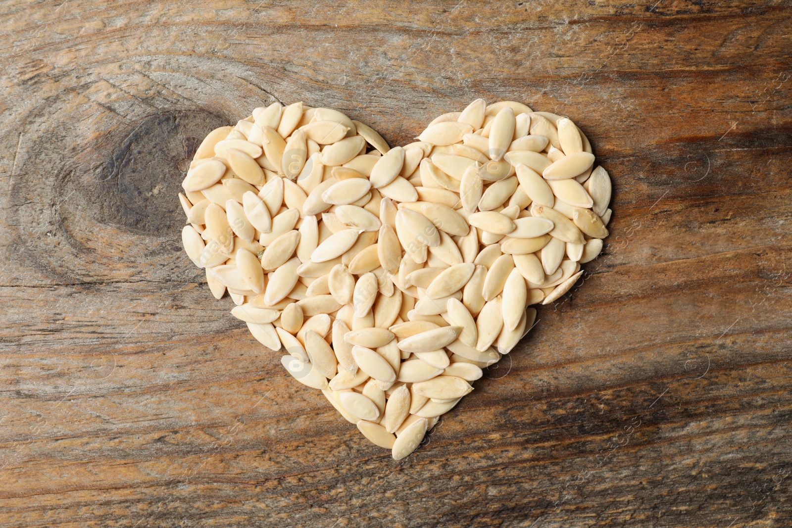 Photo of Heart made of raw cucumber seeds on wooden background, top view. Vegetable planting