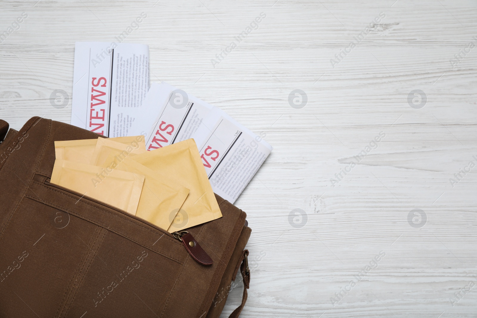 Photo of Brown postman bag with newspapers and mails on white wooden table, flat lay. Space for text