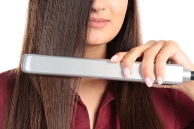 Young woman using hair iron on white background, closeup