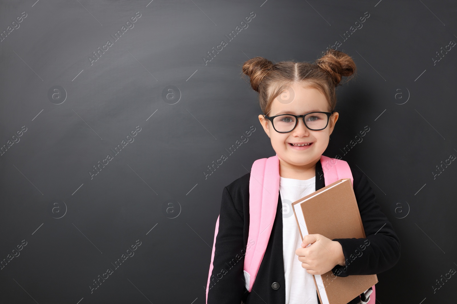 Photo of Happy little school child with book near chalkboard. Space for text