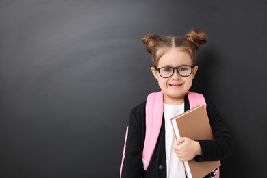 Happy little school child with book near chalkboard. Space for text