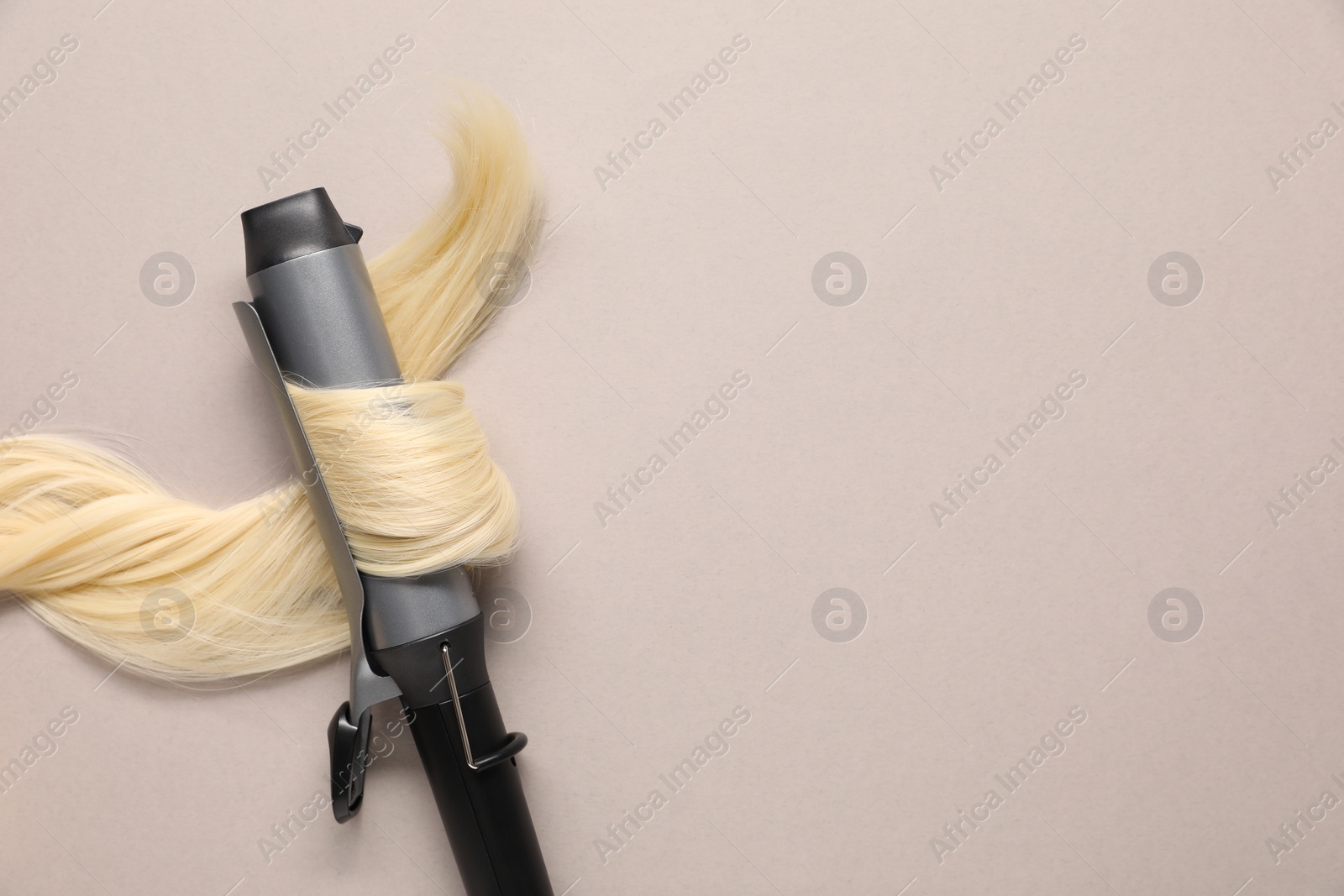 Photo of Curling iron with blonde hair lock on beige background, top view. Space for text