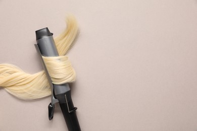 Curling iron with blonde hair lock on beige background, top view. Space for text