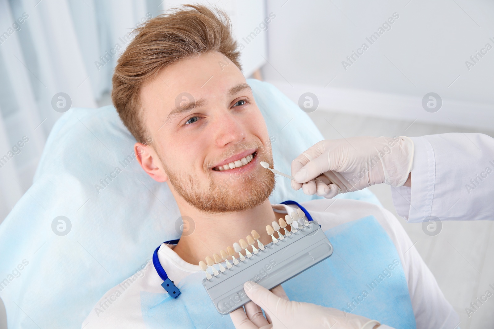 Photo of Dentist selecting patient's teeth color with palette in clinic