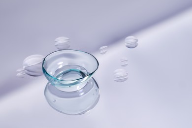 Photo of Contact lens and drops of water on light reflective surface. Space for text