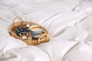 Wicker tray with cup of coffee and candles on soft white blanket