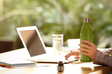 Photo of Woman with green thermos bottle at workplace, closeup. Space for text