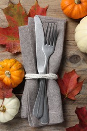 Photo of Thanksgiving table setting. Cutlery, napkin, autumn leaves and pumpkins on wooden background, flat lay