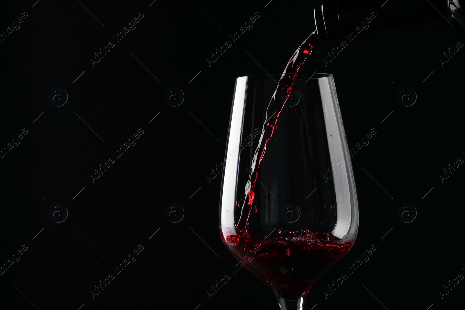 Photo of Pouring red wine into glass against black background, closeup. Space for text