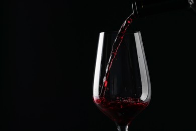 Pouring red wine into glass against black background, closeup. Space for text