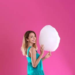 Happy young woman with cotton candy on pink background
