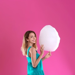 Photo of Happy young woman with cotton candy on pink background