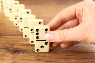 Photo of Woman putting domino tile onto wooden table to create chain reaction, closeup