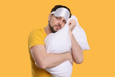 Photo of Tired man with sleep mask and pillow on yellow background. Insomnia problem