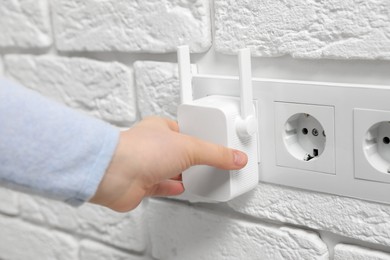 Woman turning on wireless Wi-Fi repeater indoors, closeup