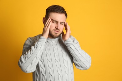 Photo of Man suffering from migraine on yellow background. Space for text