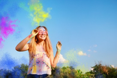 Photo of Happy woman covered with colorful powder dyes outdoors, space for text. Holi festival celebration