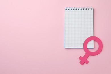 Photo of Female gender sign as women's health symbol and notebook on pink background, top view. Space for text