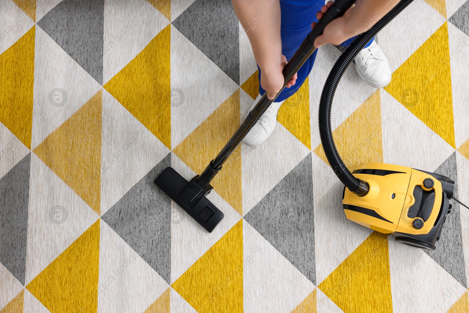 Photo of Dry cleaner's employee hoovering carpet with vacuum cleaner, above view