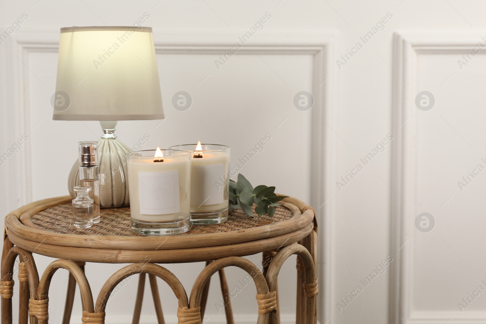 Photo of Burning soy candles, lamp, perfumes and eucalyptus branch on wicker table indoors. Space for text