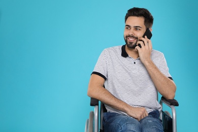 Young man in wheelchair talking on phone against color background. Space for text