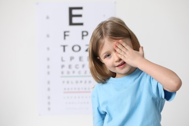 Photo of Little girl covering her eye against vision test chart