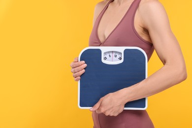 Photo of Slim woman holding scales on yellow background, closeup and space for text. Weight loss
