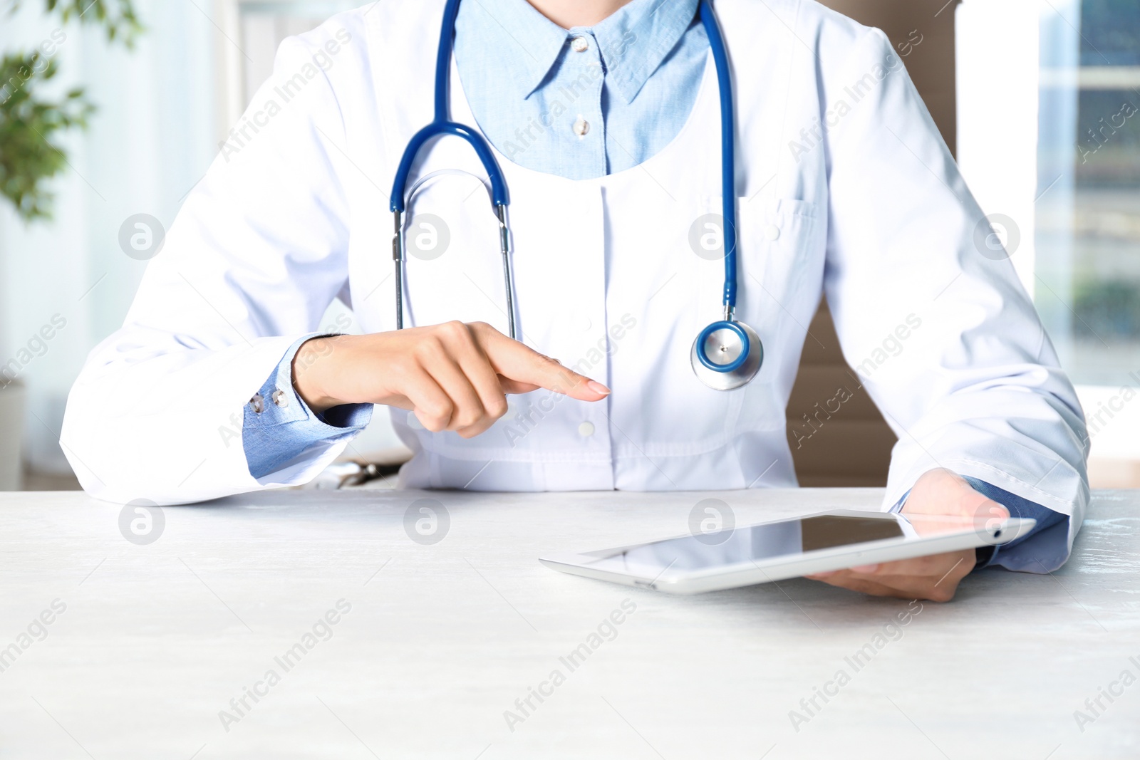 Photo of Female doctor with modern tablet sitting at table indoors, closeup