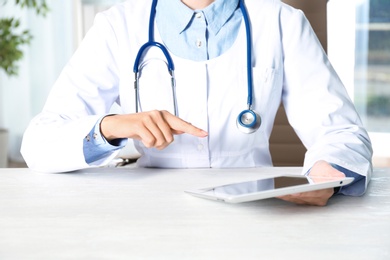 Female doctor with modern tablet sitting at table indoors, closeup