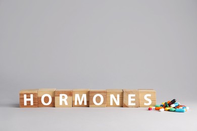 Photo of Word HORMONES made with wooden cubes and pills on grey background. Space for text