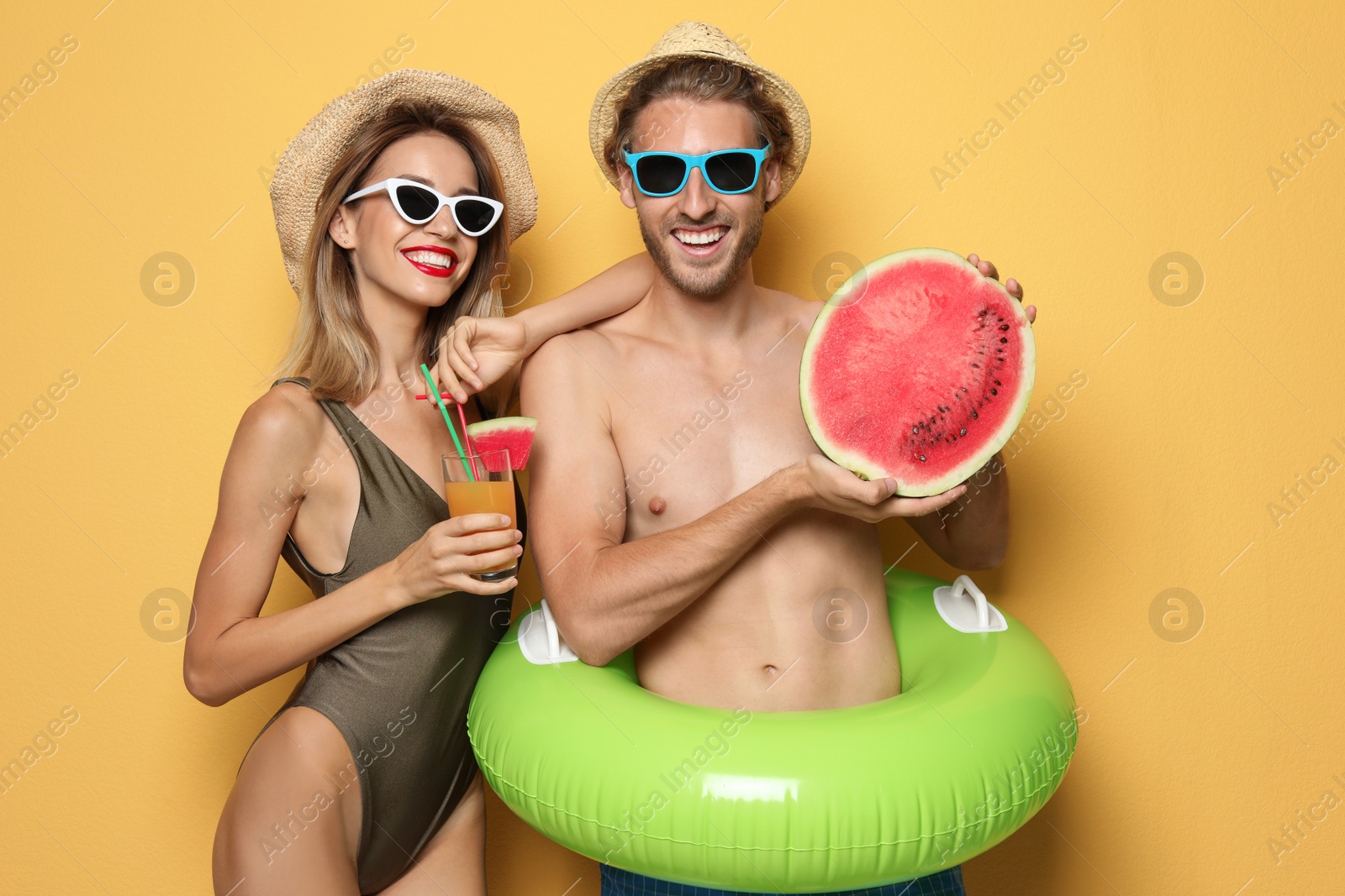 Photo of Happy young couple in beachwear with inflatable ring and cocktail on color background