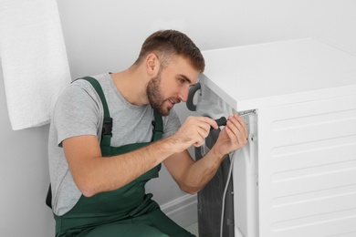 Photo of Young plumber fixing washing machine in bathroom