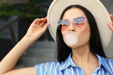 Photo of Stylish woman blowing gum near building outdoors