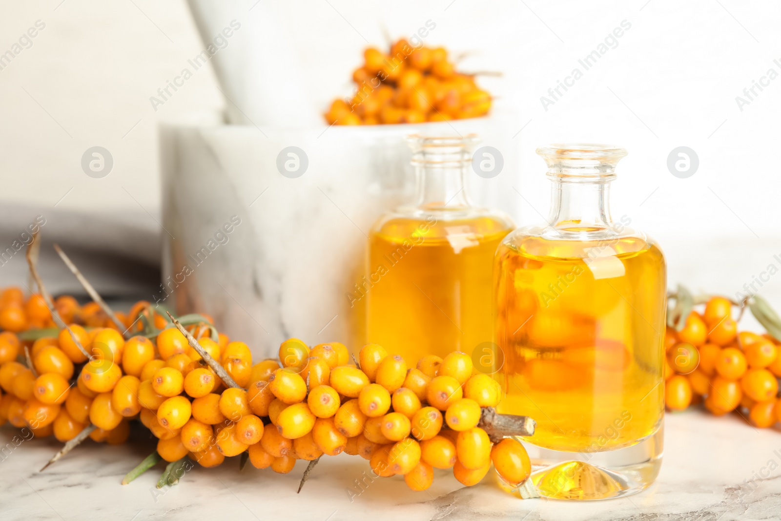 Photo of Natural sea buckthorn oil and fresh berries on white marble table