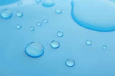 Drops of spilled water on light blue background, closeup