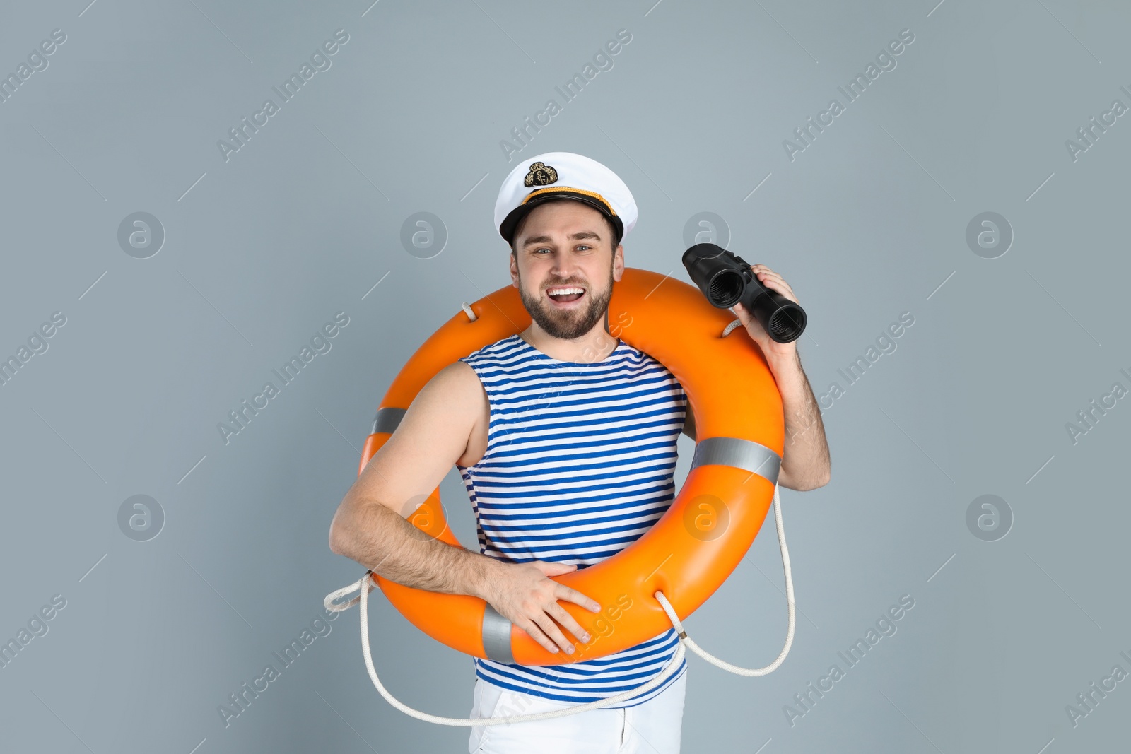 Photo of Happy sailor with binoculars and ring buoy on light grey background