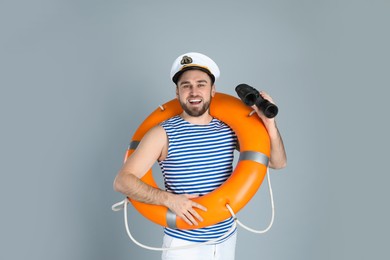 Photo of Happy sailor with binoculars and ring buoy on light grey background