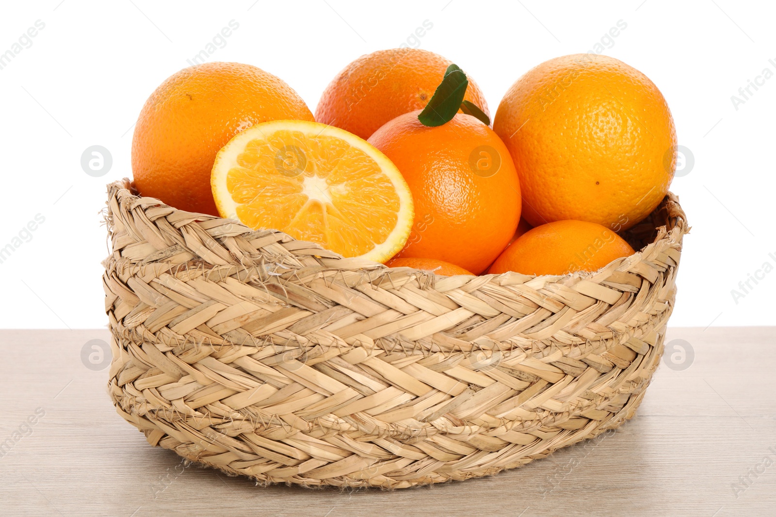 Photo of Fresh oranges in wicker basket on light wooden table against white background