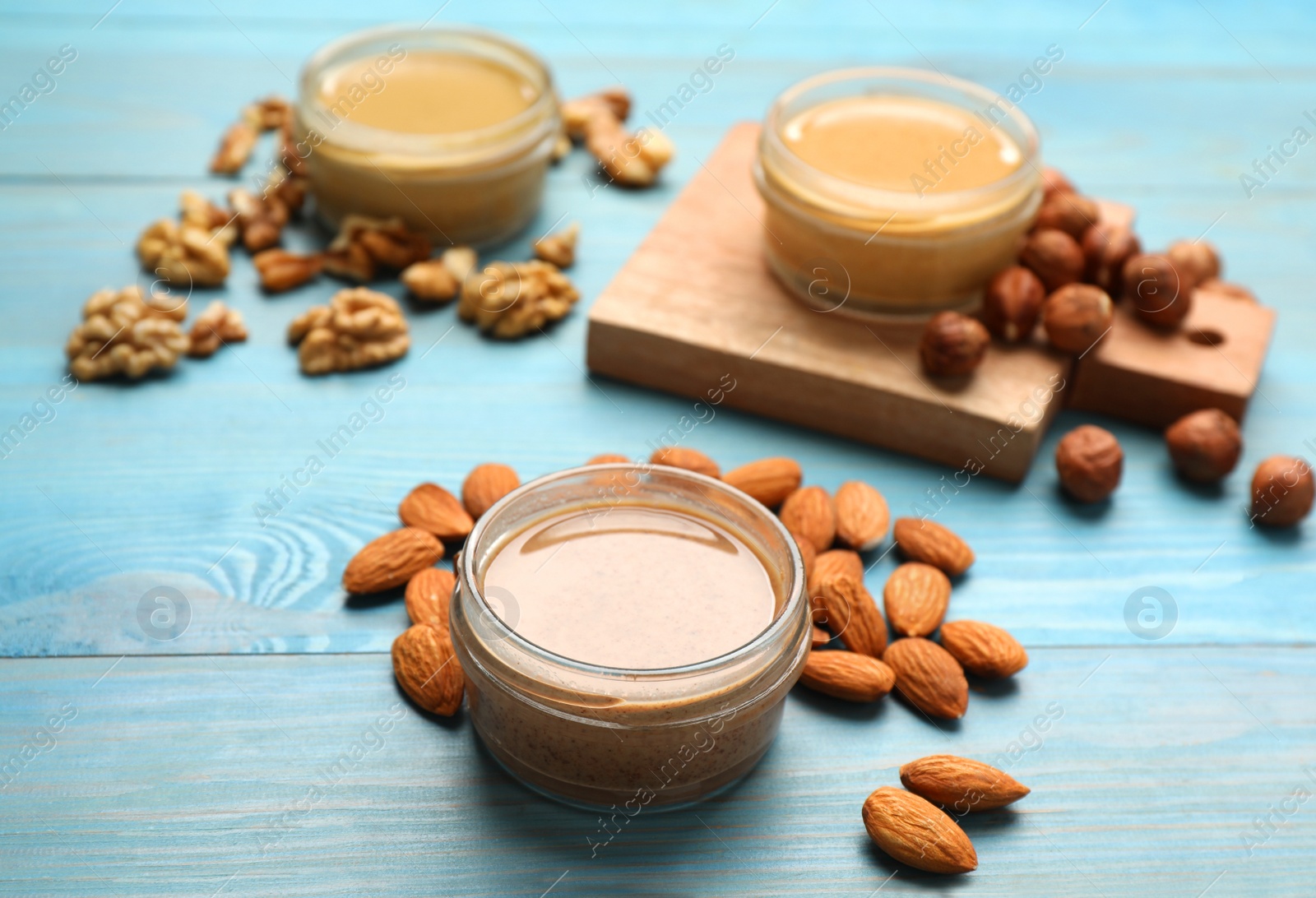 Photo of Different types of delicious nut butters and ingredients on light blue wooden table, closeup