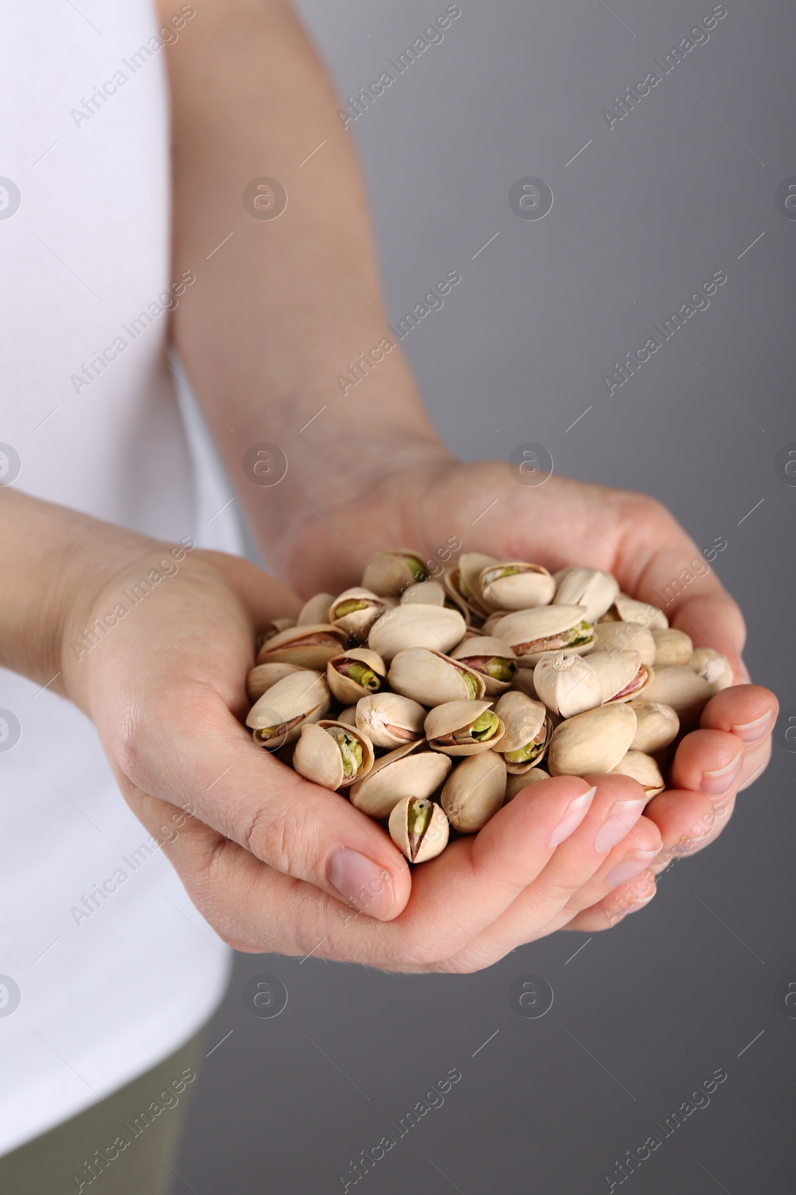 Photo of Woman holding handful of tasty pistachios on grey background, closeup